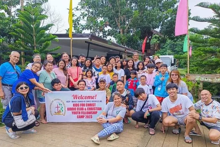 A large group of children and adults posing with a Welcome banner for a Kids for Christ and youth fellowship camp in 2023