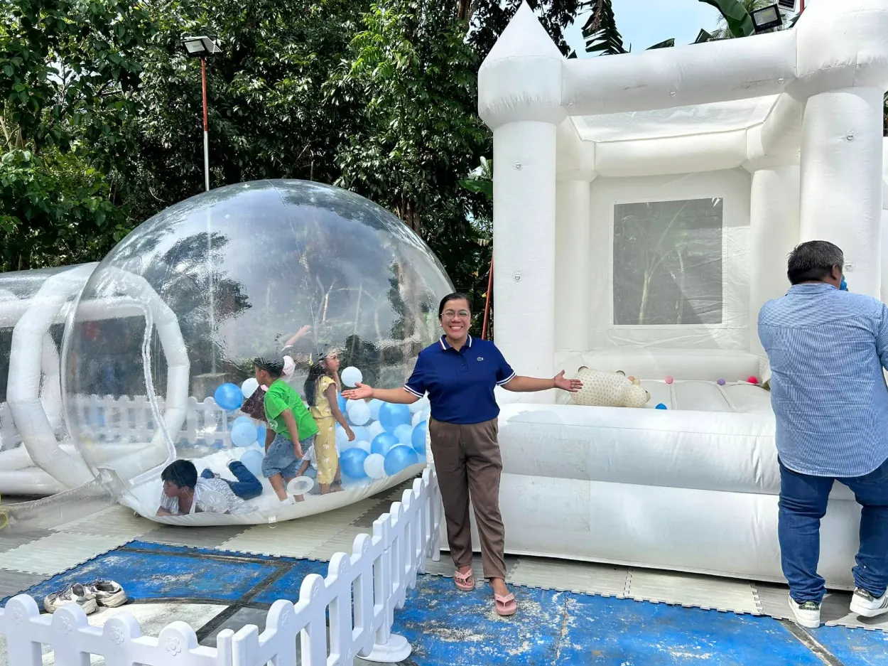 Children playing inside a clear bubble house with balloons next to a white bounce house